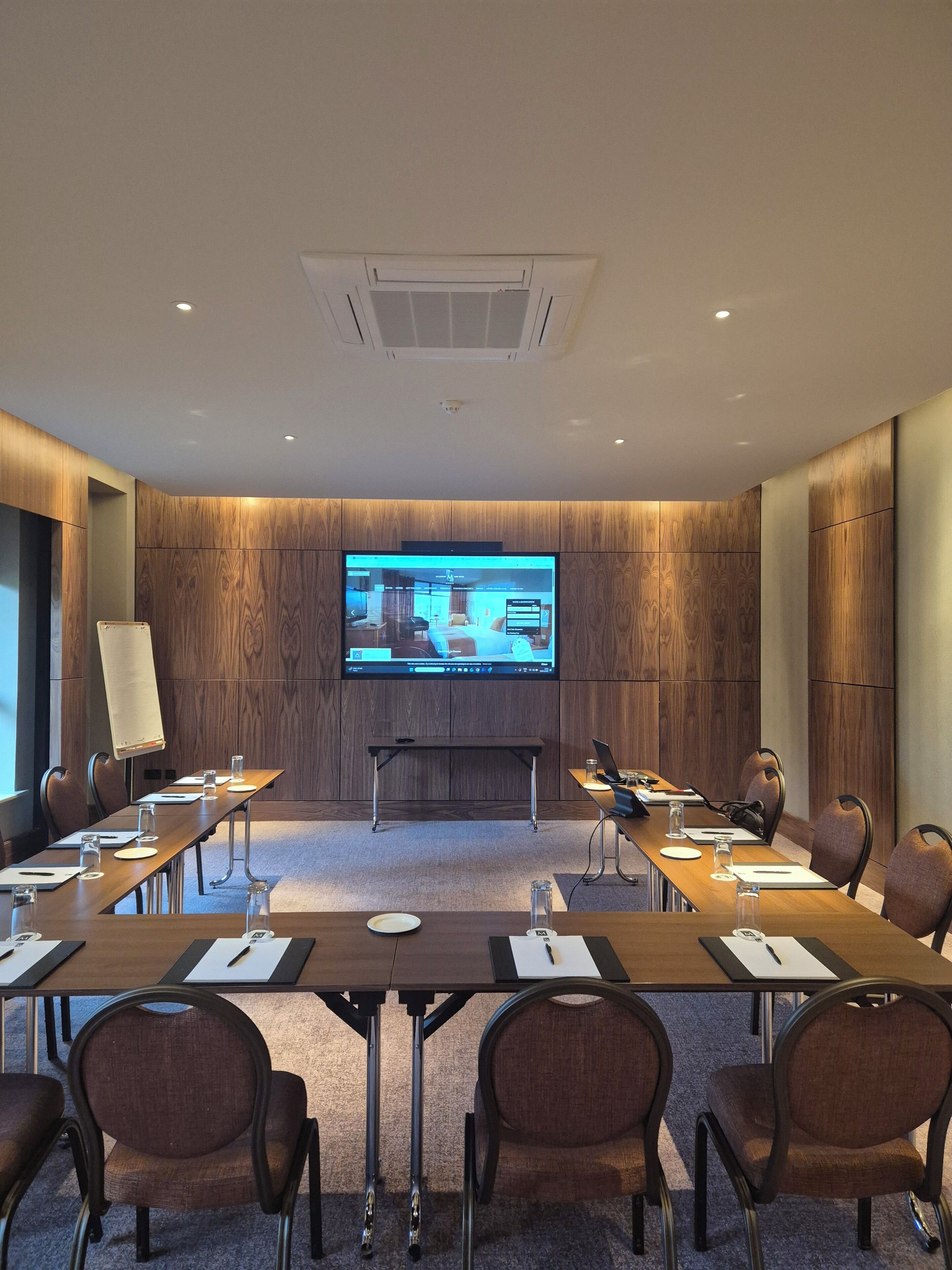 A conference room with a large screen, wooden panel walls, and a carpeted floor.