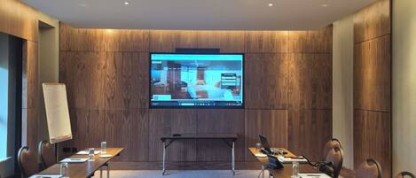 A conference room with a large screen, wooden panel walls, and a carpeted floor.
