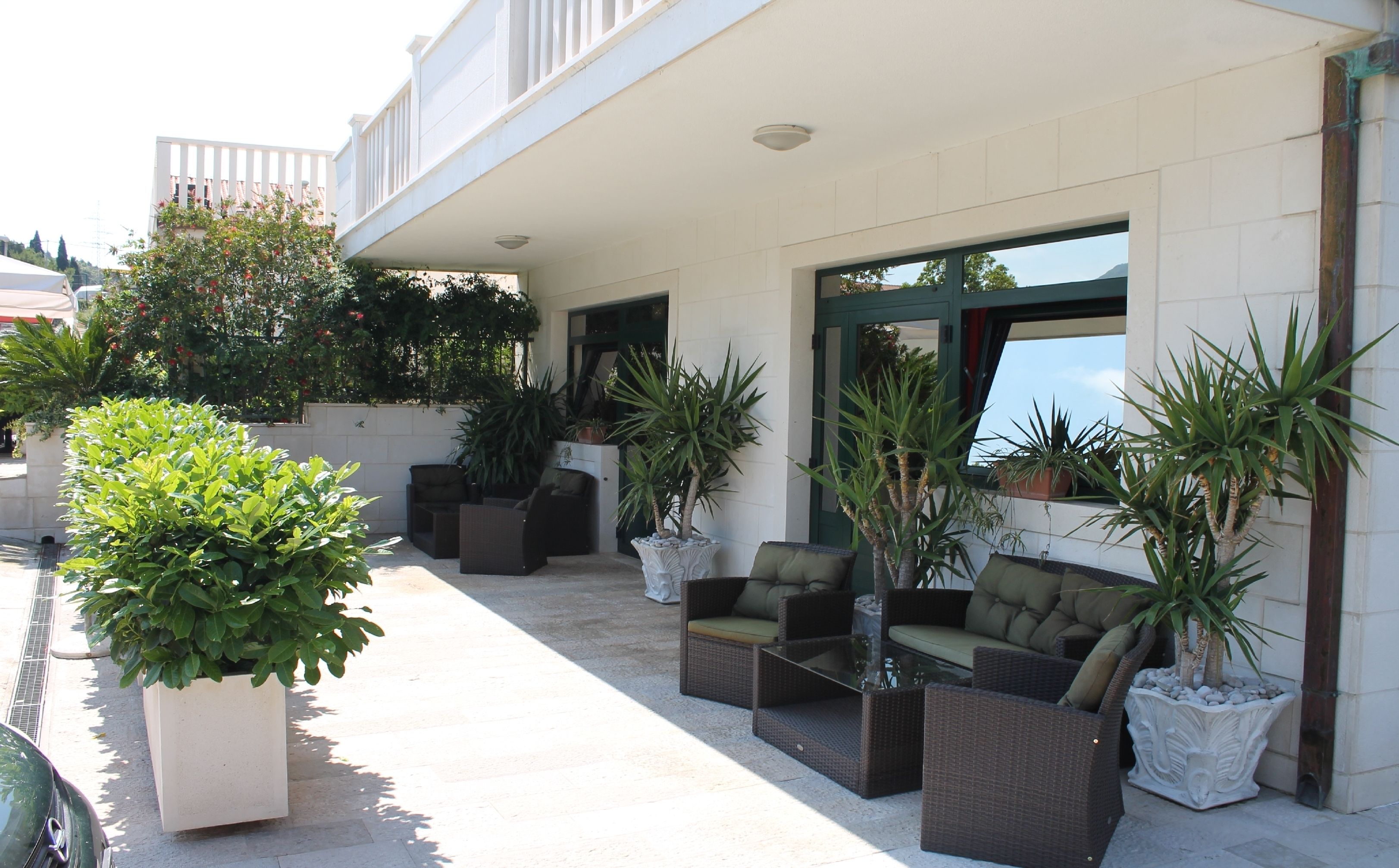 An outdoor seating area with wicker furniture, potted plants, and a view of the sea.