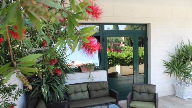 A patio with a sofa and chairs, surrounded by potted plants and a green door. - Apartments Logoš Cavtat (Konavle)