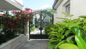 A gated entrance with a metal gate, a concrete pathway, and lush green plants on either side. - Apartments Logoš Cavtat (Konavle)