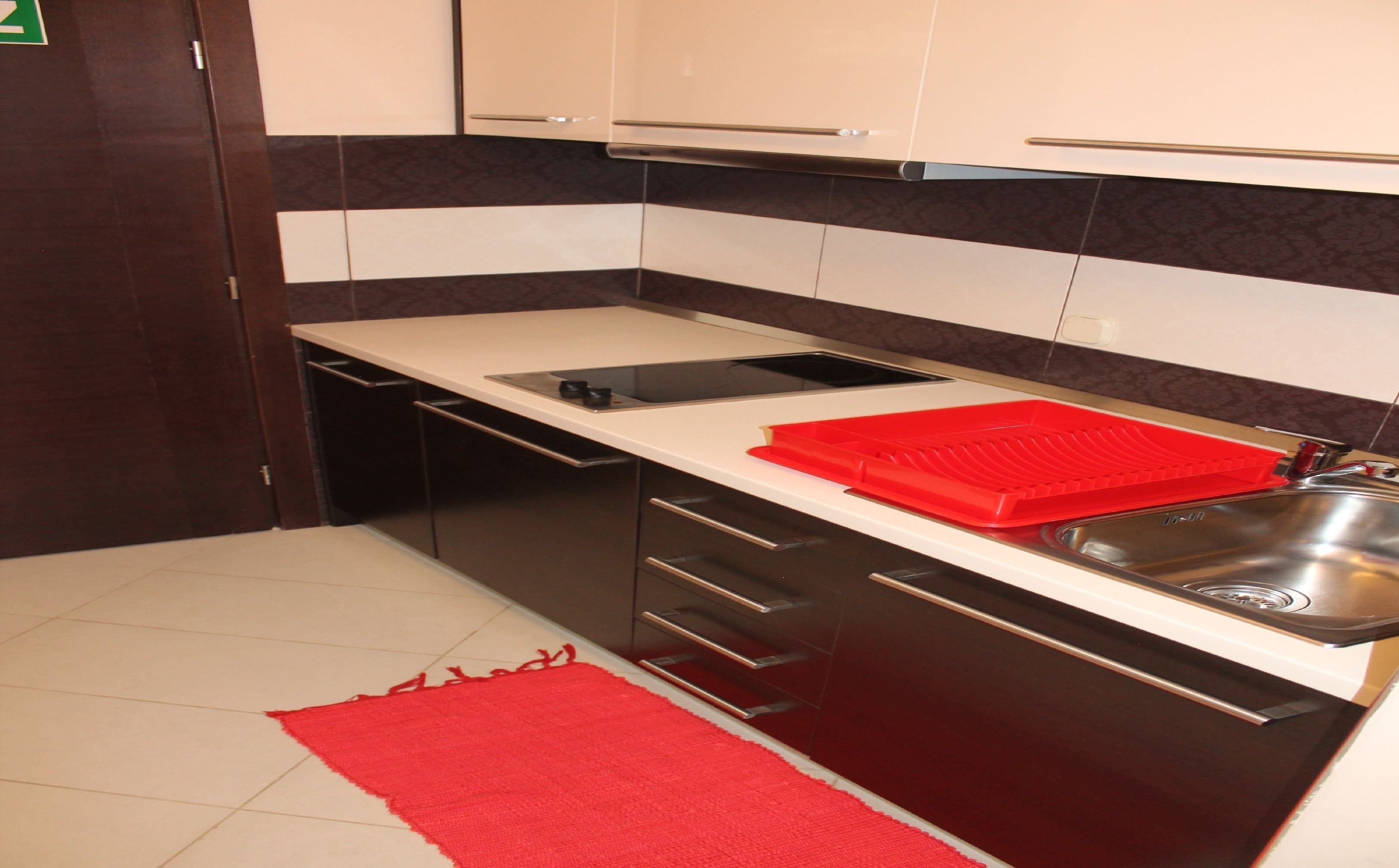 A compact kitchen with dark cabinetry, a white countertop, a red cutting board, and a stainless steel sink.