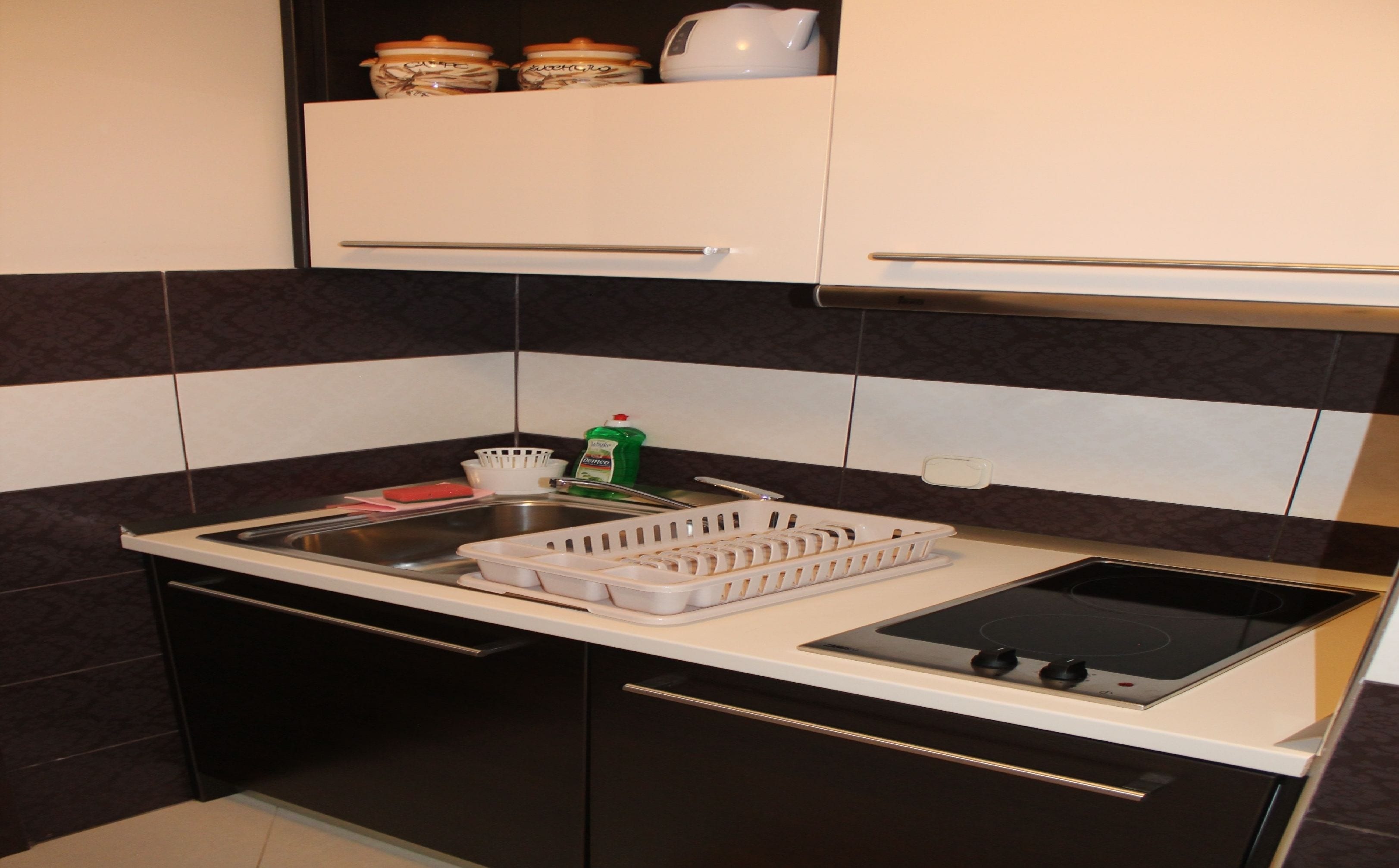 A compact kitchen with a black and white tiled backsplash, a stainless steel sink, and a stove with a black cooktop.