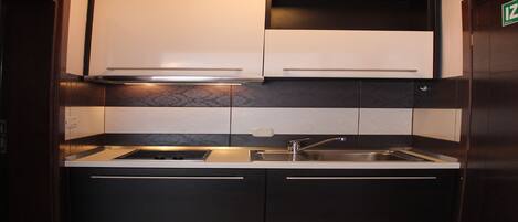Una cocina compacta con estufa integrada, un lavabo y armarios superiores.