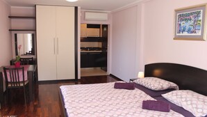 A hotel room with a bed, a desk, a chair, a wardrobe, a kitchenette, and a framed picture on the wall. - Apartments Logoš Cavtat (Konavle)