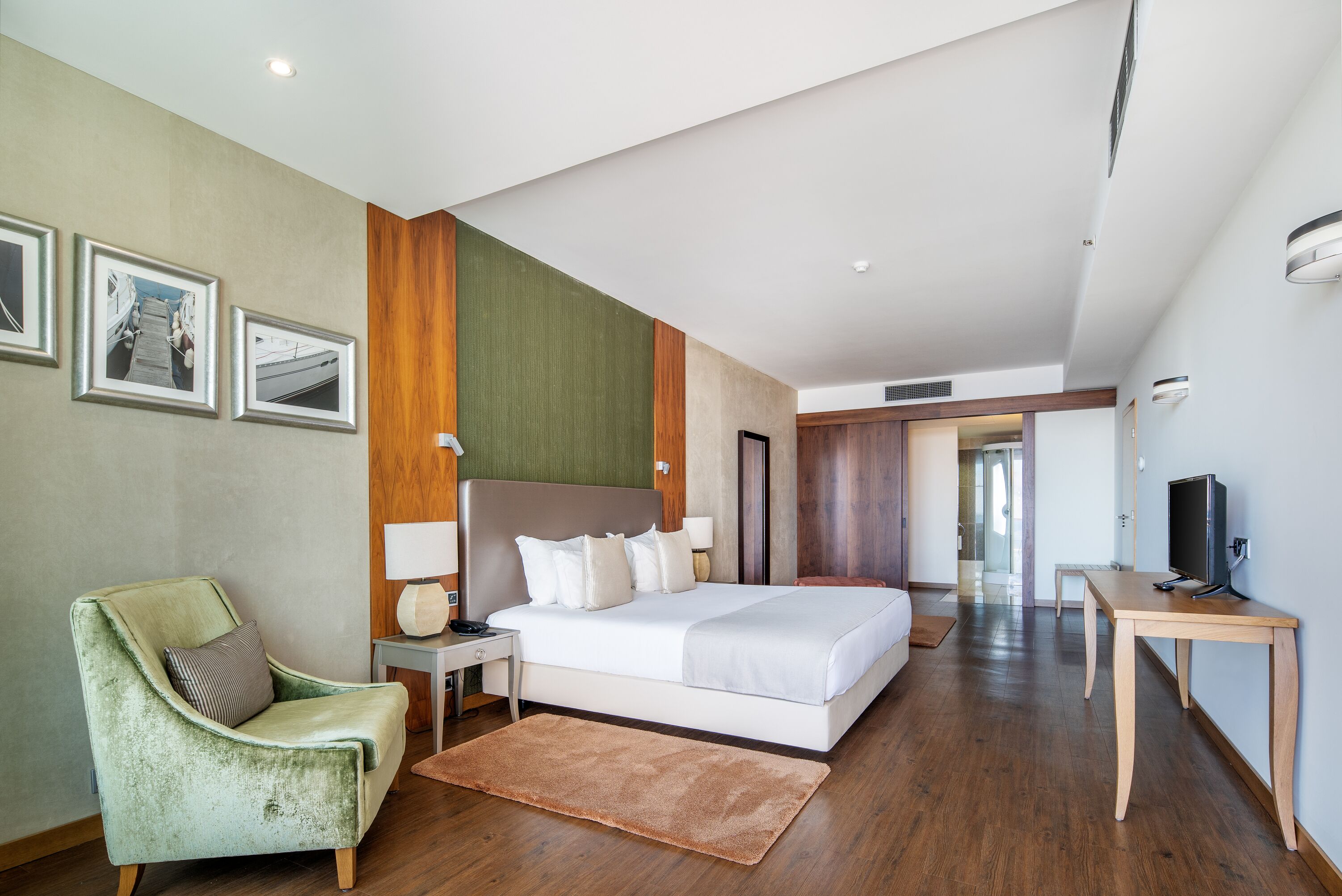 Una habitación de hotel moderna con una cama, un sillón verde, un escritorio y un televisor.