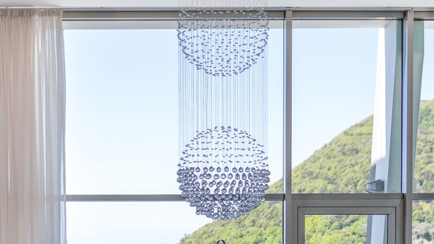 A teal sofa with a tufted backrest and two pillows, positioned in front of a large window with a view of the sea and a mountainous landscape. - Angra Marina Hotel (Angra do Heroismo)