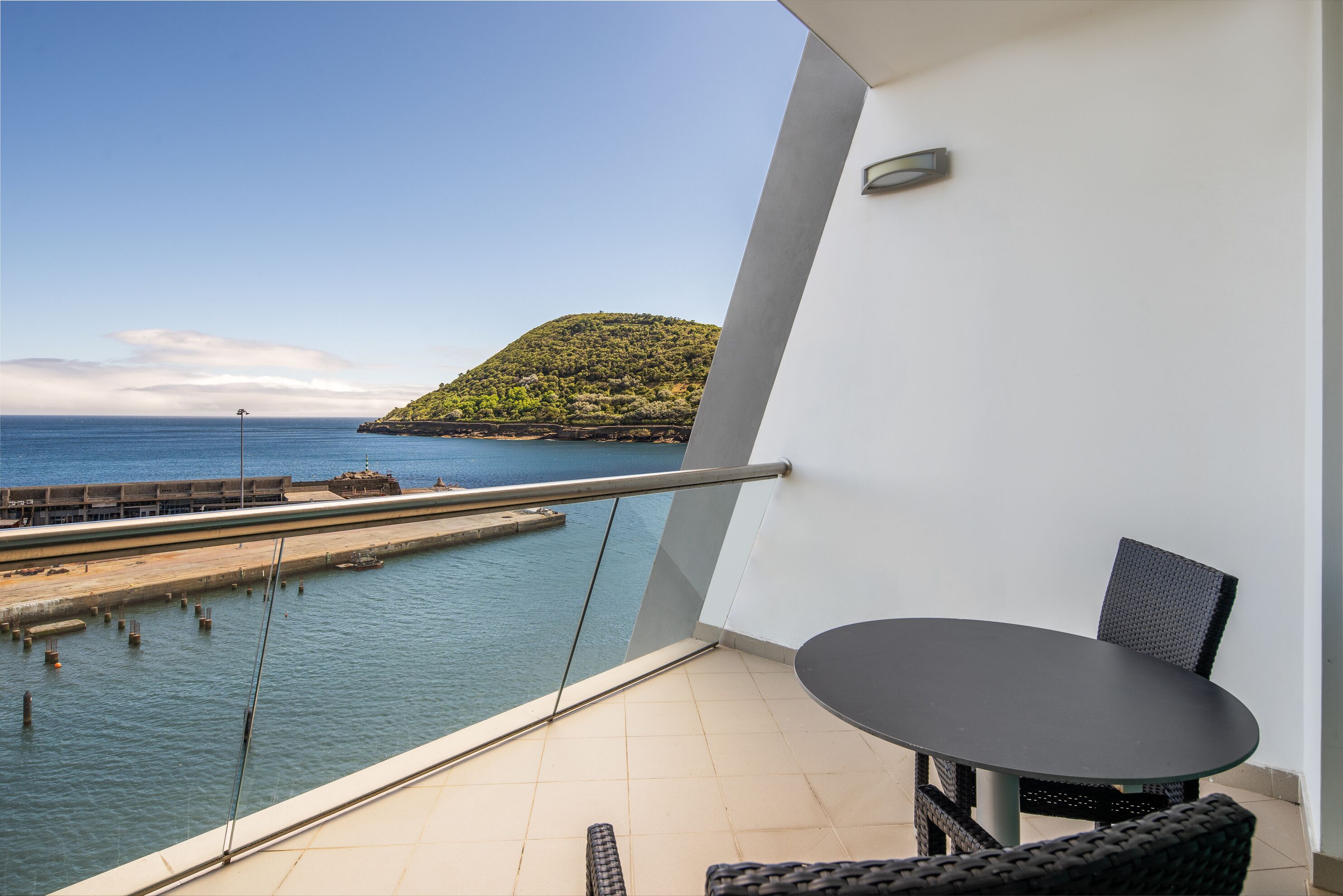 A balcony with a view of the sea and a distant hill.