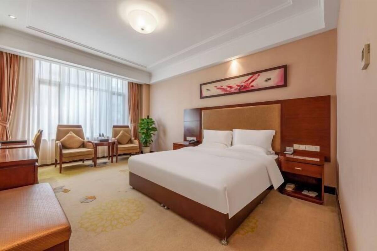 Une chambre d’hôtel avec un grand lit, un bureau, deux chaises, une table de chevet et une plante en pot.