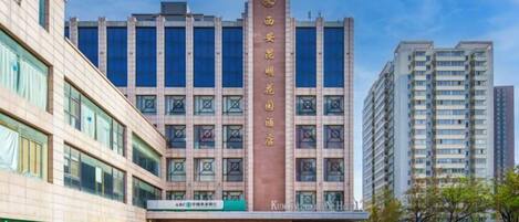 Um edifício com vários andares, uma placa vertical chamativa, janelas amplas e um telhado plano.