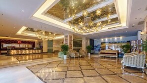 Un hall d’entrée spacieux avec un sol en marbre poli, un espace d’accueil avec une enseigne rouge et un coin salon avec des canapés et des fauteuils.