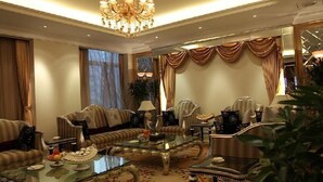 Un salon luxueux agrémenté d’un lustre, de canapés, d’une table basse en verre et de rideaux drapés.