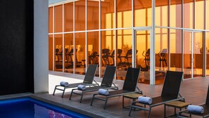 Una piscina interior con sillas de descanso y equipo de ejercicios visibles a través de amplios ventanales.