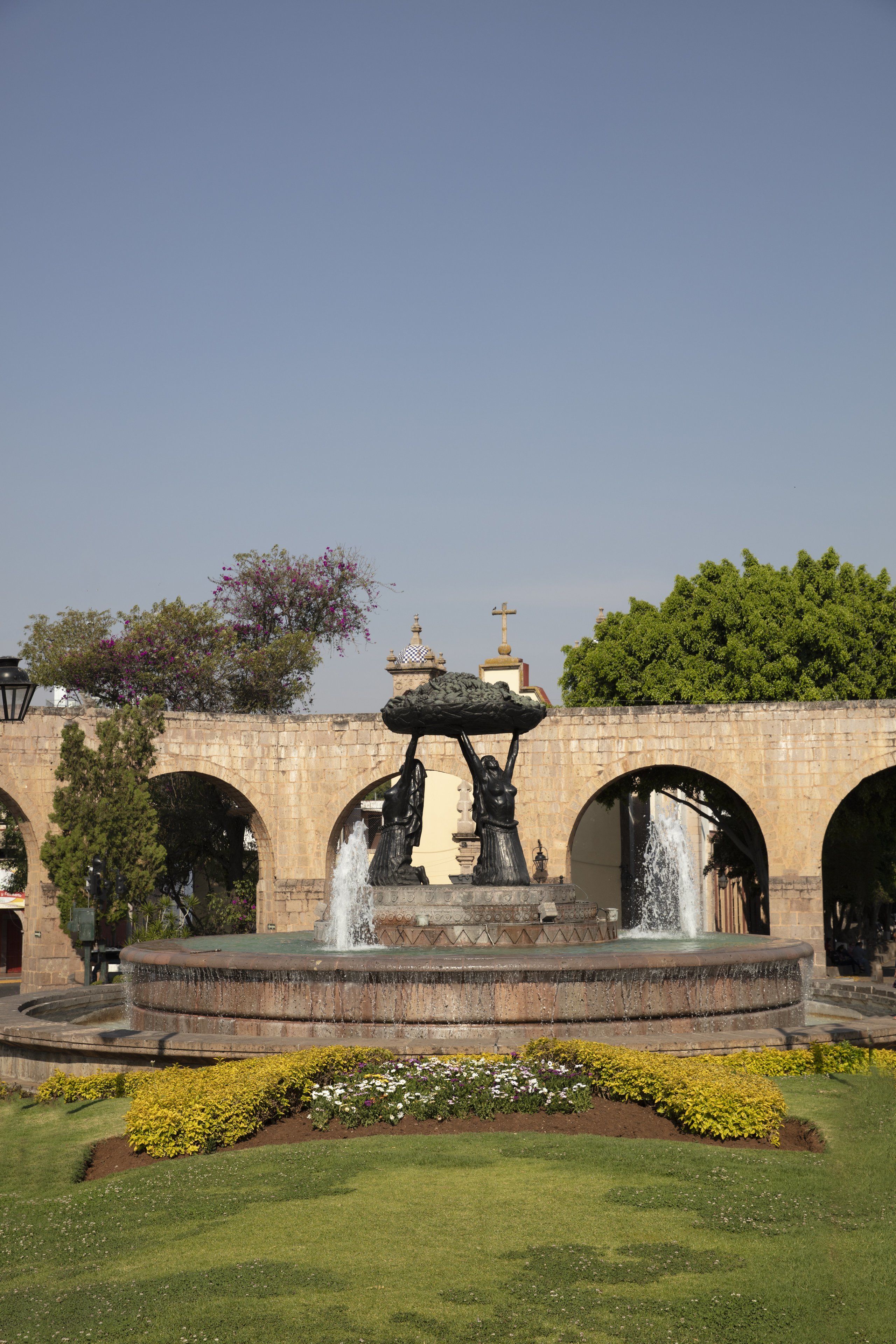Una fuente con chorros de agua, rodeada de césped cuidado y macizos de flores.