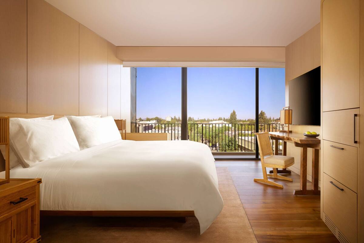 A modern bedroom with a large bed, a desk, and a TV.