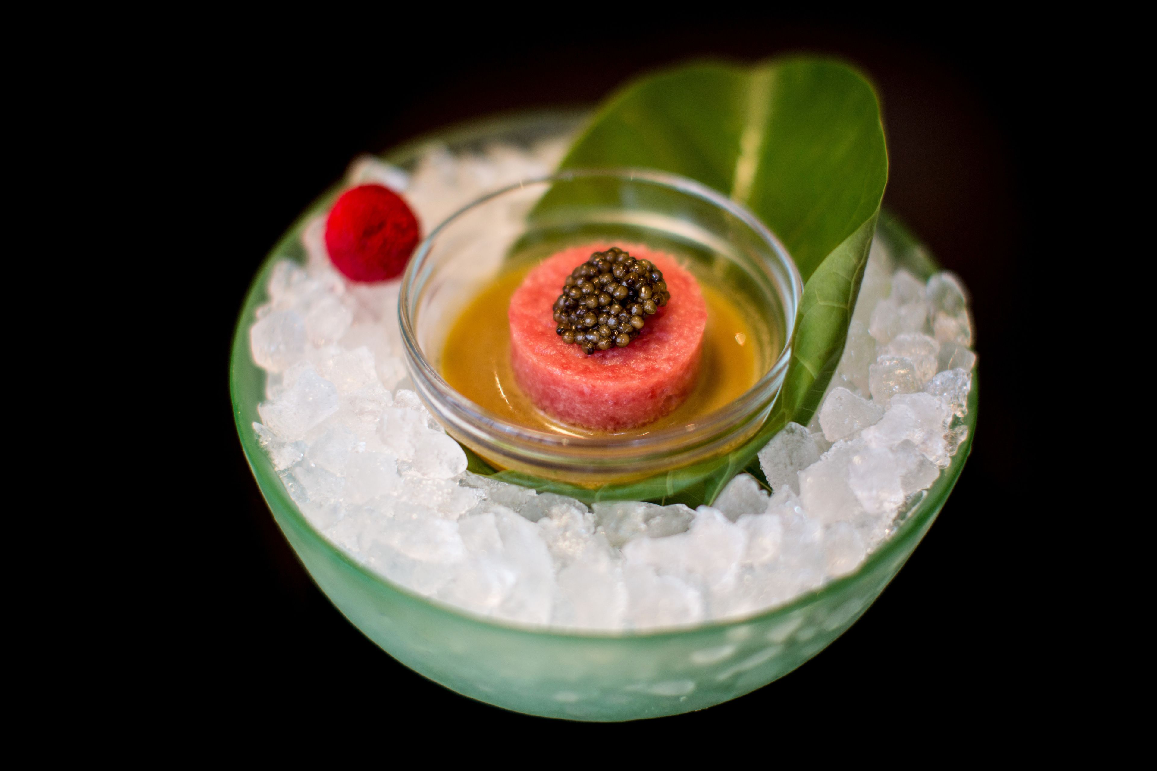 Un postre con un centro de fruta esférica, rodeado de hielo y decorado con una baya y una hoja.