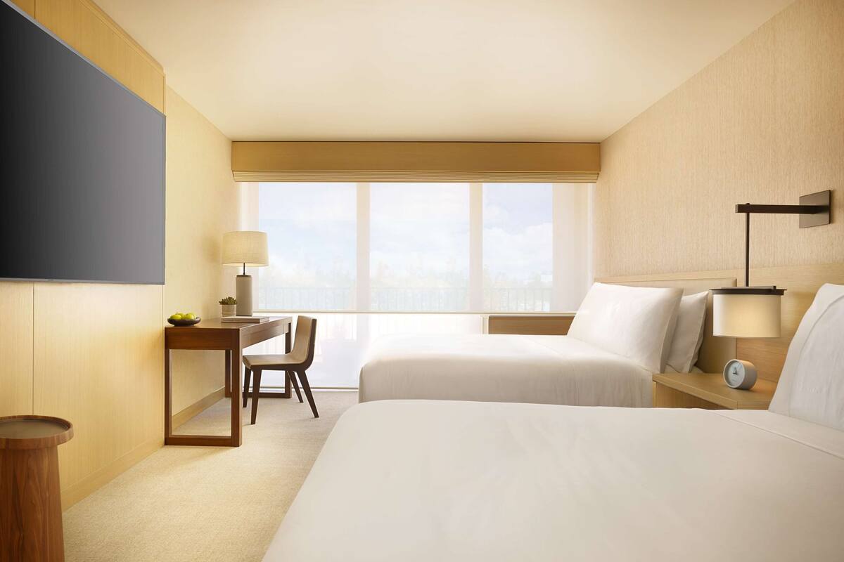 Una habitación de hotel con una cama grande, un escritorio con silla, una mesita, una lámpara y un reloj en la mesita de noche.