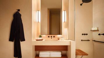 Un baño moderno con un espejo grande, un lavamanos, una ducha y una bata colgada en la pared.