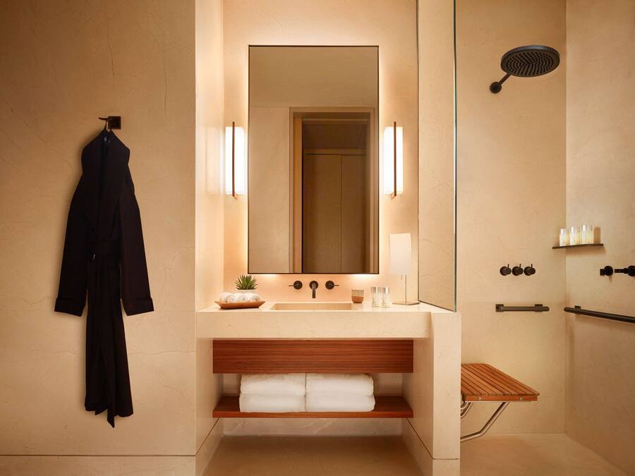 Un baño moderno con un espejo grande, un lavamanos, una ducha y una bata colgada en la pared.