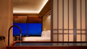 Una habitación de hotel moderna con una cama grande, vistas al cielo nocturno, una bañera de madera y un balcón con barandilla.