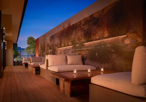A modern outdoor seating area with sofas and tables, a large mural on the wall, and a wooden deck. - Nobu Hotel Palo Alto (Palo Alto)