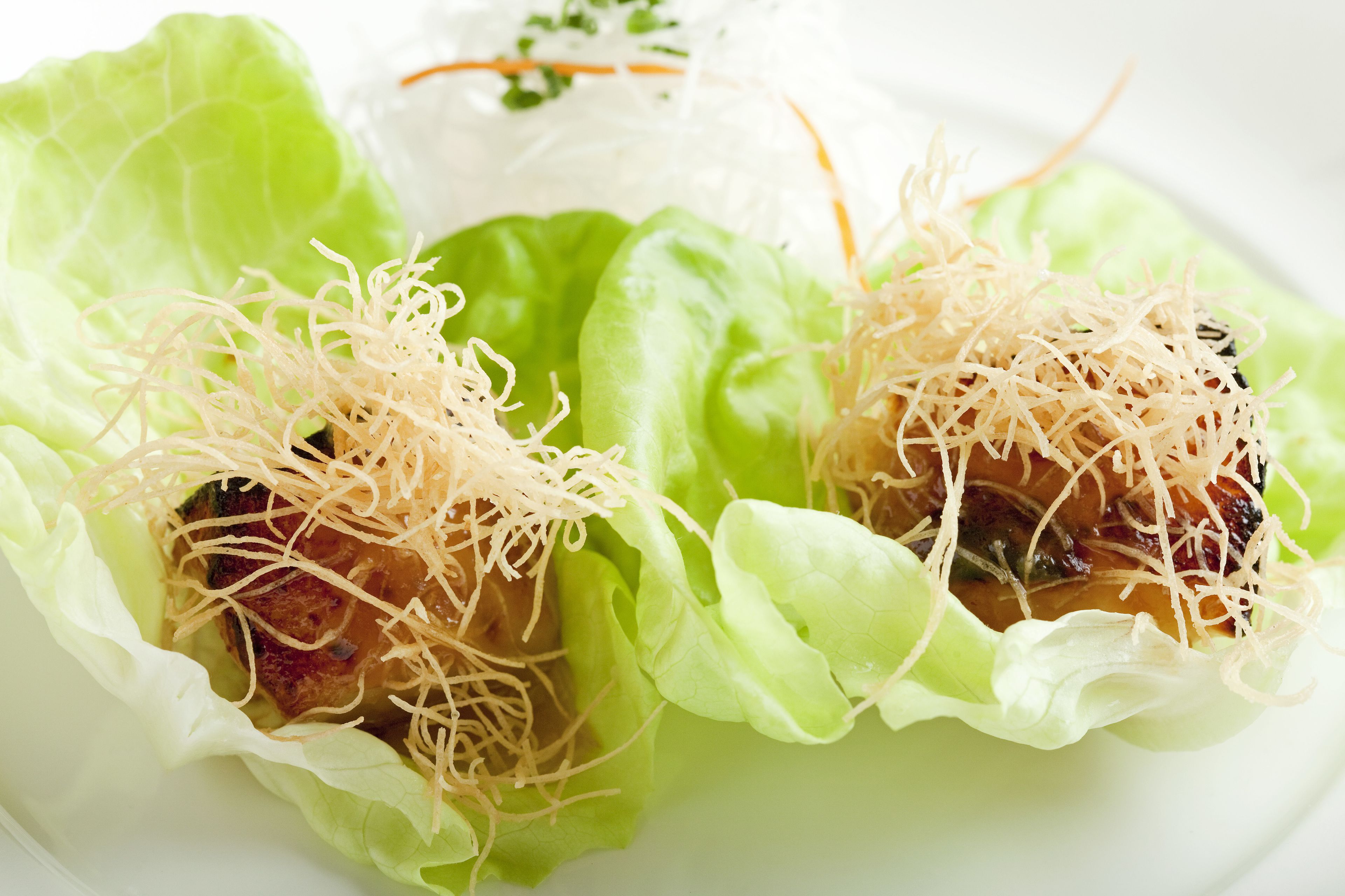 A plate with two food items wrapped in lettuce leaves, garnished with shredded toppings.