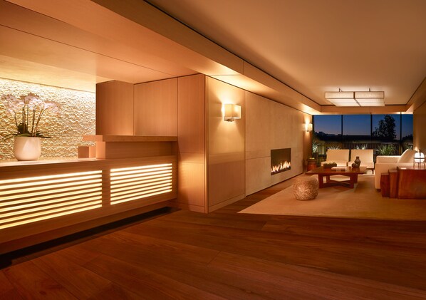 A modern interior with a wooden reception desk, a fireplace, and a seating area with a view of the outdoors.