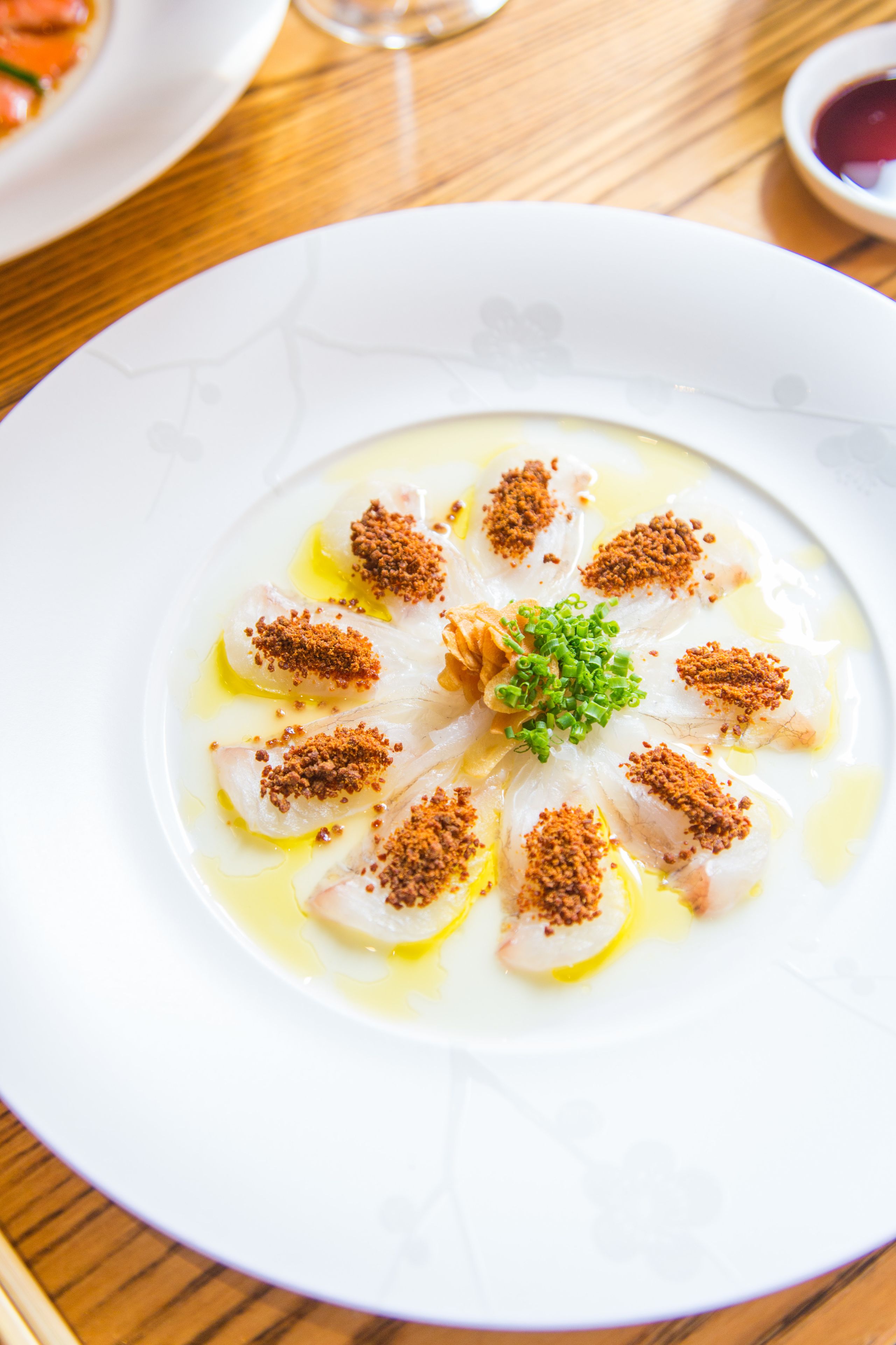 A white plate with a seafood dish, garnished with green onions and brown spices, on a wooden table.