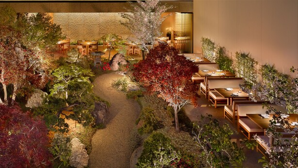 Un restaurante con terraza rodeado de un sendero ajardinado y diversas plantas.