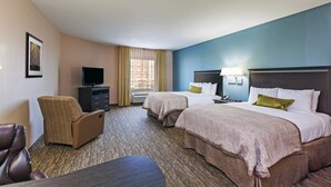Quarto de hotel com duas camas, uma escrivaninha, uma cadeira, uma televisão e uma janela com cortinas.
