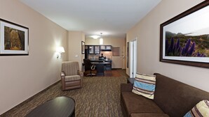 Quarto de hotel com área de estar, escrivaninha e cozinha compacta.