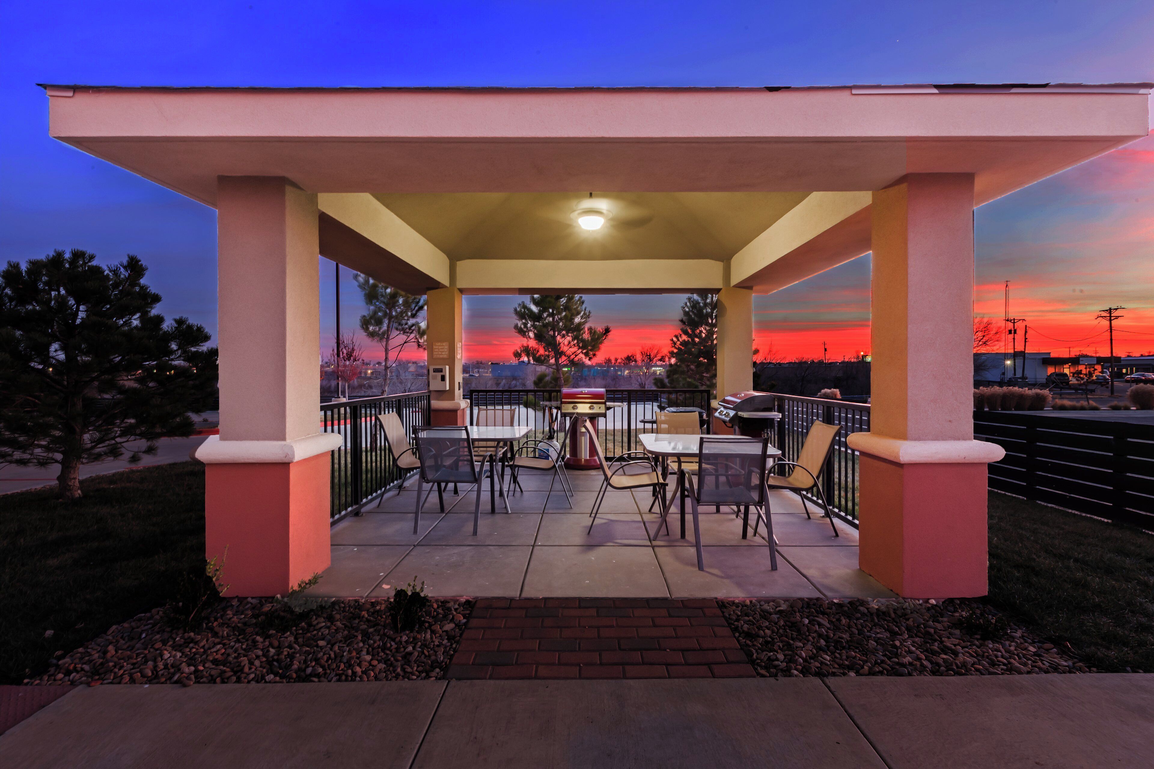 An outdoor patio with tables and chairs, a barbecue grill, and a view of the city skyline at sunset.