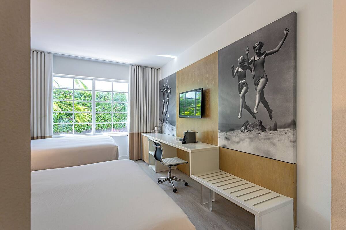Ein modernes Hotelzimmer mit einem großen Bett, einem Schreibtisch, einem Sessel, einem Fernseher und Bildern an den Wänden.
