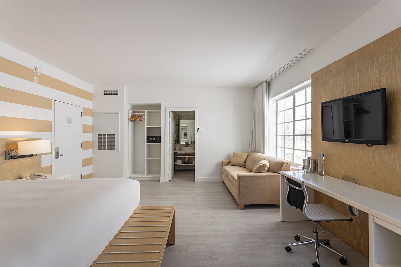 Hotelkamer met een bed, een bureau met stoel, een bank, een televisie en een badkamer met spiegel en wastafel.