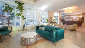 Een ruime lobby met een blauwgroene bank, een rond bijzettafeltje en een hangstoel.