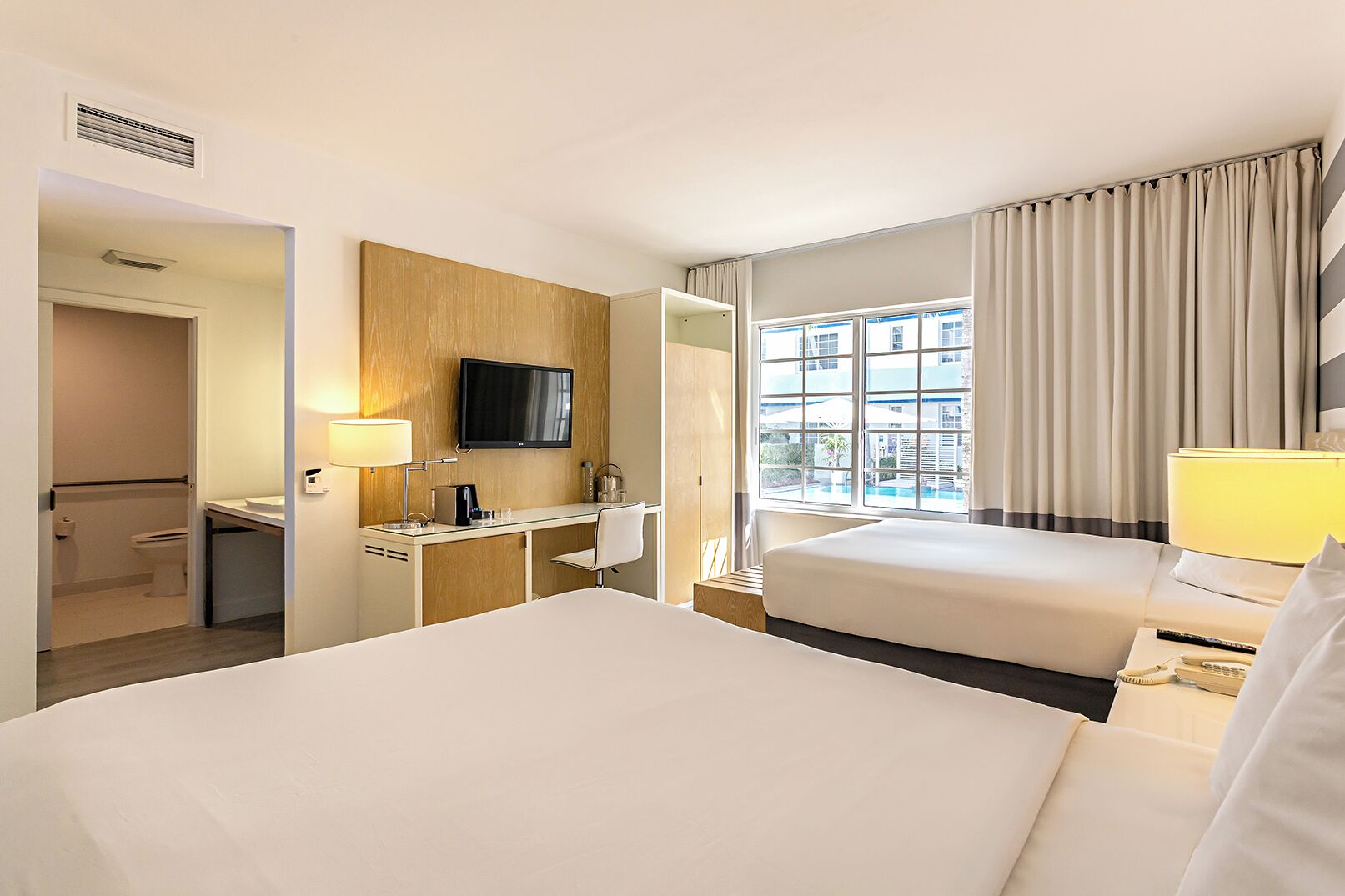 A hotel room with a bed, desk, TV, and a window with curtains.