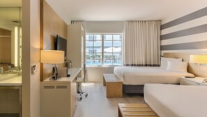 Een hotelkamer met een bed, nachtkastje, lamp, bureau met stoel en een raam met gordijnen.