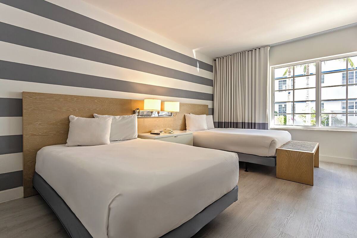 Ein Hotelzimmer mit einem großen Bett, Nachttischen, Vorhängen an einem Fenster und Blick auf Gebäude.
