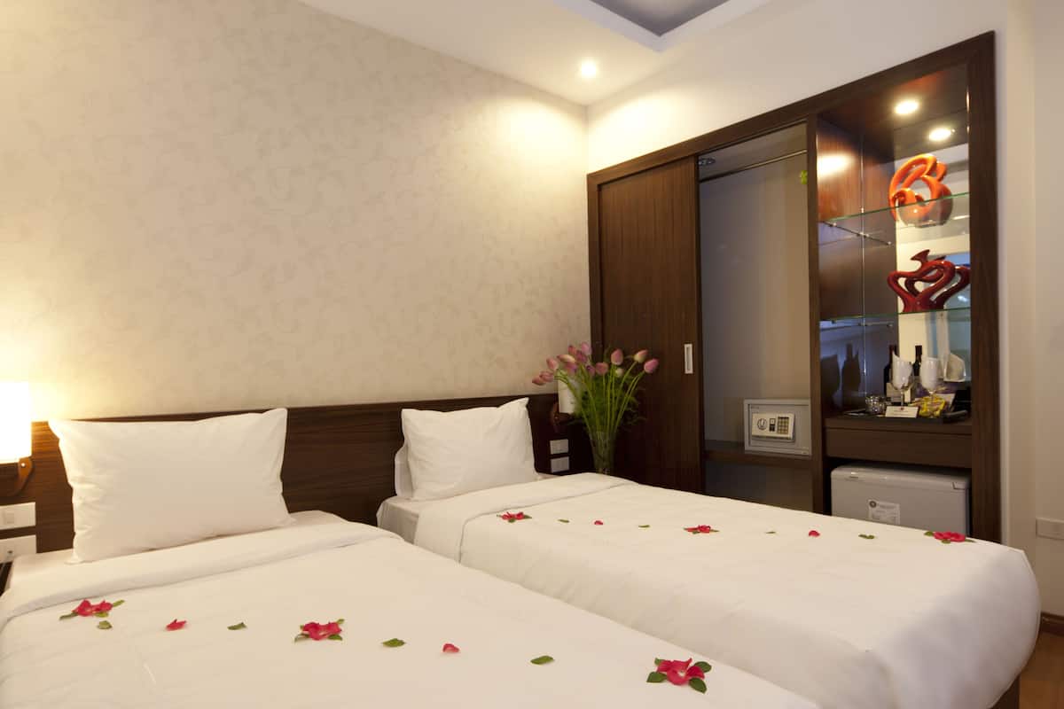 A hotel room with two beds, a wooden wardrobe, a small refrigerator, and a decorative item on the wall.