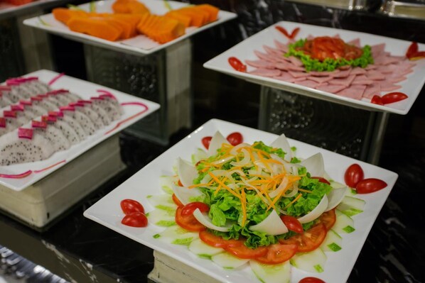 A buffet with various dishes including a salad with lettuce, tomatoes, and shredded carrots.