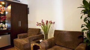 A living room with a brown sofa set, a glass coffee table, a decorative vase with flowers, and a small refrigerator. - Rising Dragon Legend Hotel (Hanoi)