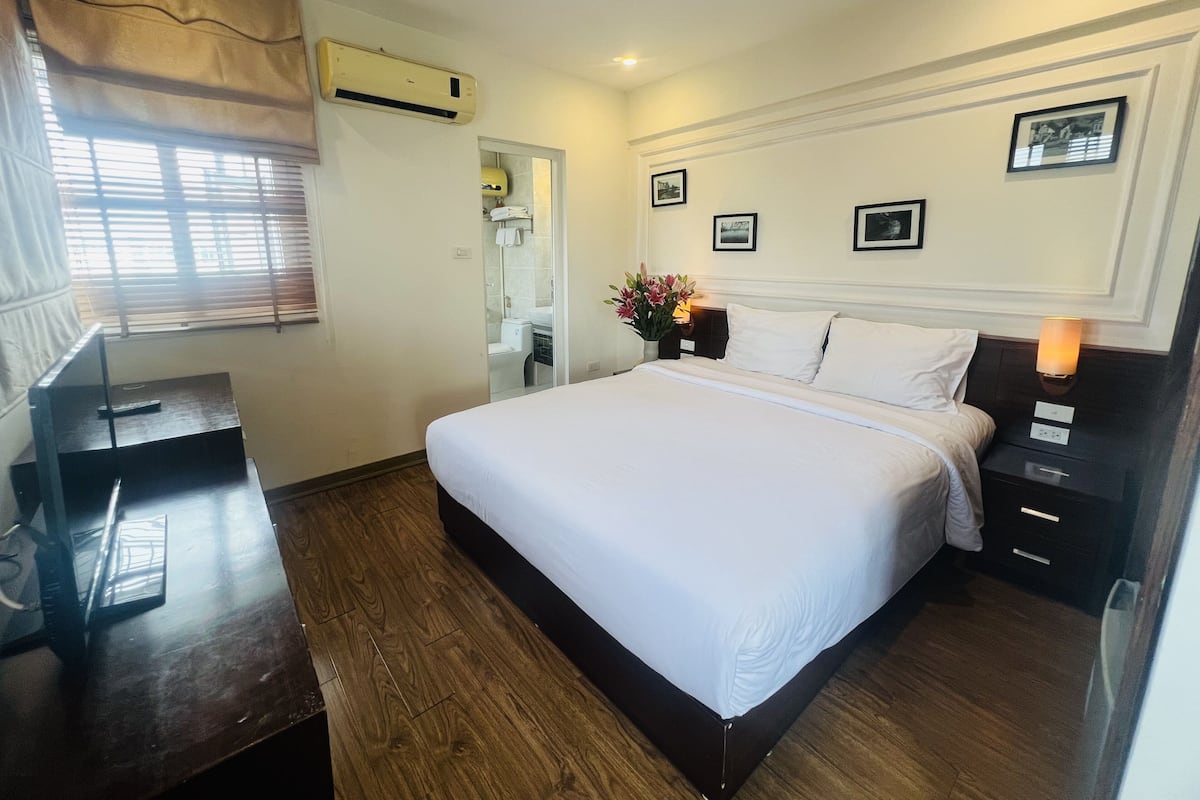 A hotel room with a large bed, a desk, an air conditioning unit, and a bathroom visible through a door.