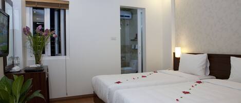 A hotel room with two beds, a potted plant, a desk, and a window with blinds.