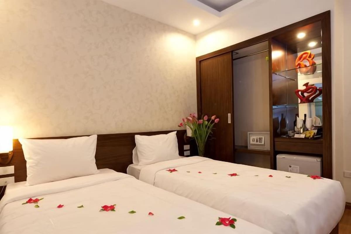 A hotel room with two beds, a nightstand, a mirror, and a vase of flowers.