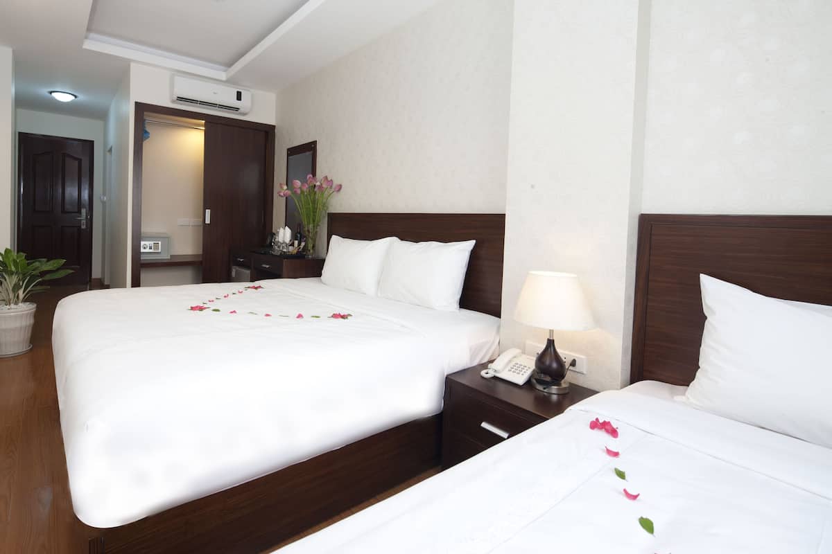 A hotel room with two beds, a bedside table with a lamp, a telephone, and a potted plant.