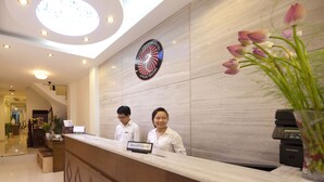 A hotel reception area with a modern design, a reception desk, and a logo on the wall. - Rising Dragon Legend Hotel (Hanoi)