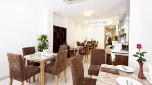 A dining area with multiple tables and chairs, a counter with a vase of flowers, and a mirror on the wall. - Rising Dragon Legend Hotel (Hanoi)