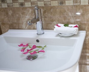 A bathroom sink with a chrome faucet, a basin, and a towel with rose petals.