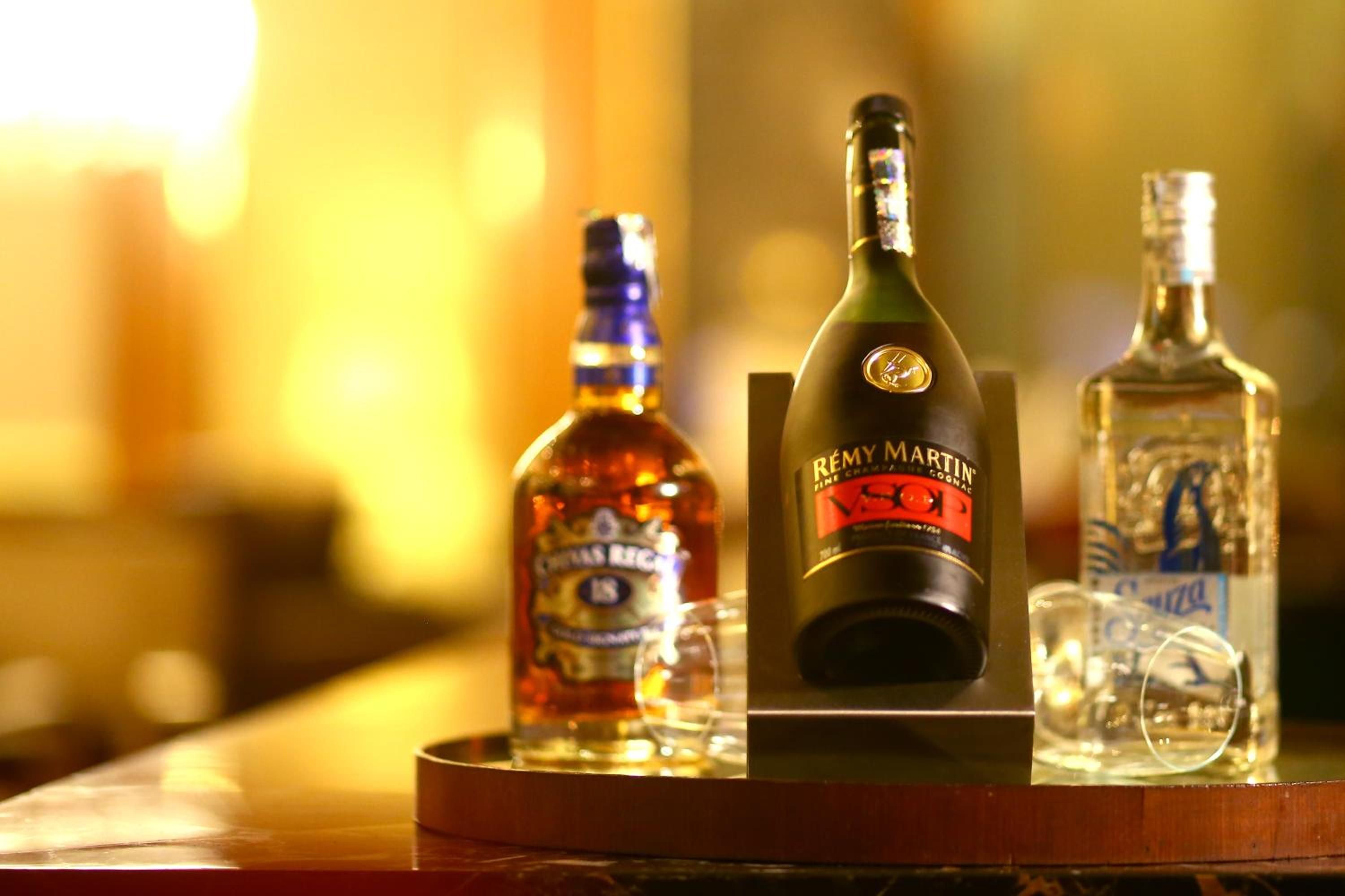 A bottle of Rêmy Martin cognac, a bottle of whiskey, and a glass on a wooden surface.