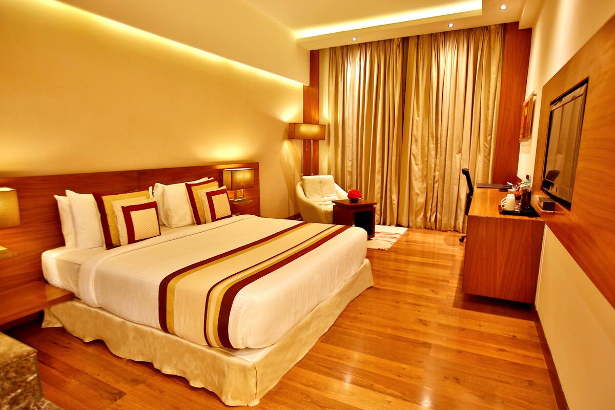 A hotel room with a large bed, a desk, a chair, and a TV.